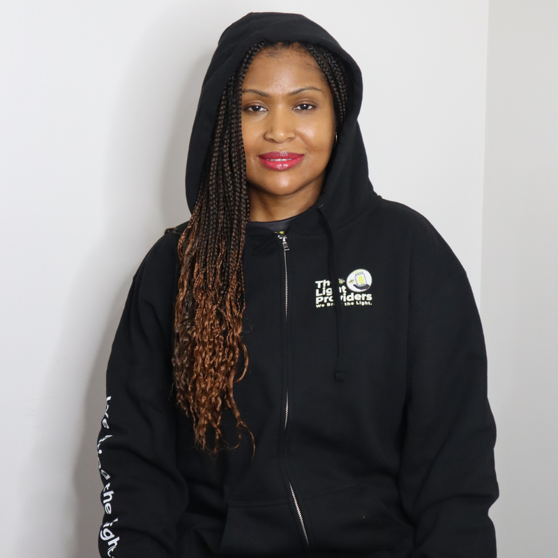 Model shown in a detail view of the print, wearing a black zip hoodie featuring The Light Providers logo patch on the ches...
