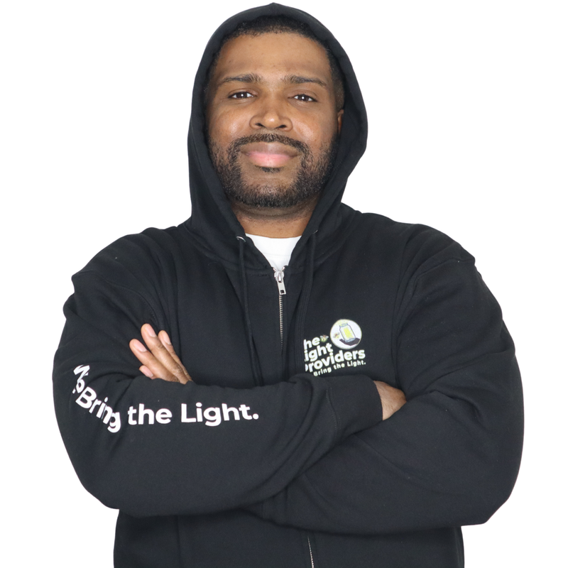Model shown in side profile, wearing a black zip hoodie featuring The Light Providers logo patch on the chest and We Bring...