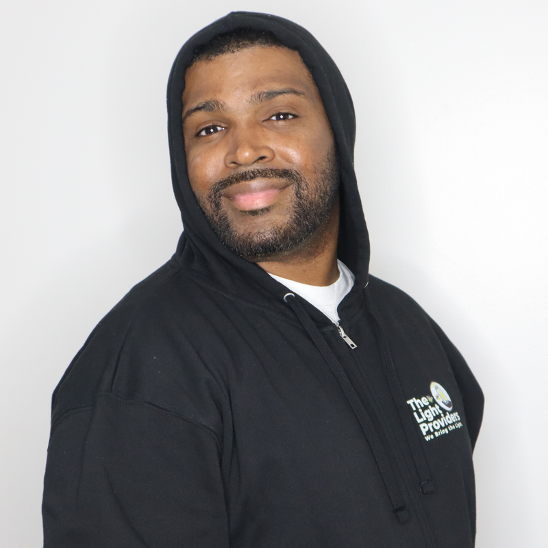Model shown close up, wearing a black zip hoodie featuring The Light Providers logo patch on the chest and We Bring the Li...