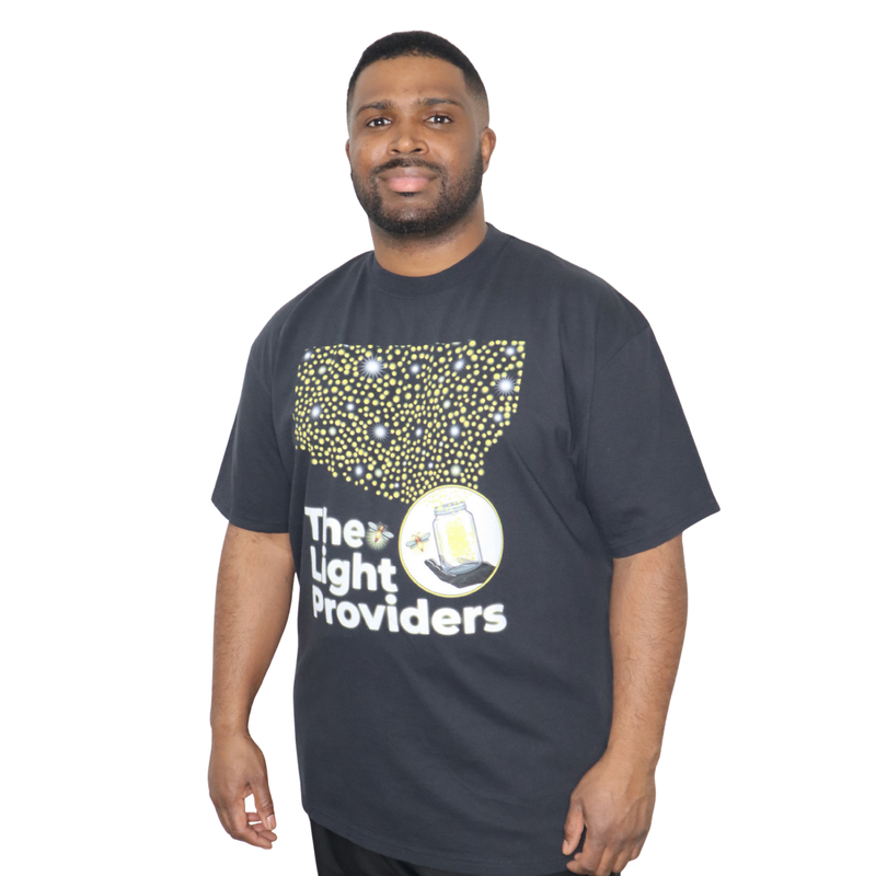 Model shown close up, wearing a garment dyed t-shirt featuring a scattered firefly light pattern above The Light Providers...