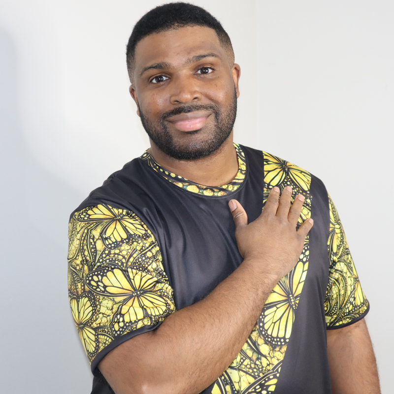 Model shown close up, wearing a t-shirt featuring a yellow monarch butterfly Ankara style print sash across a black tee