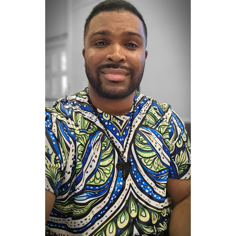 Model shown with arms crossed, wearing a t-shirt featuring an all over green white and blue Ankara style leaf pattern