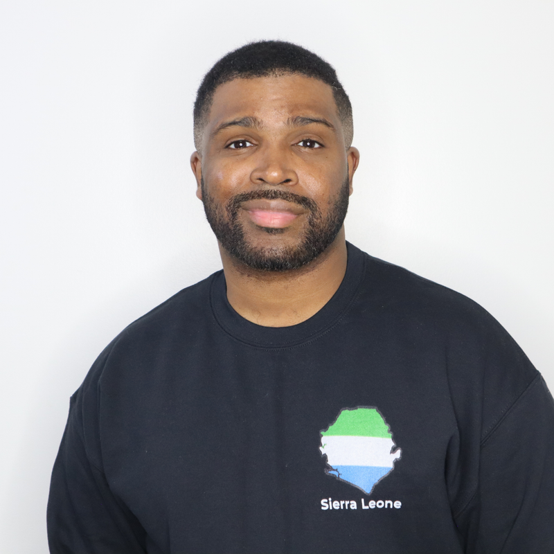 Model shown close up, wearing a black crewneck sweatshirt featuring a Sierra Leone text and country outline map print in g...