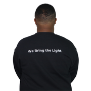 Person wearing a black sweatshirt with 'We Bring the Light' text on the back.