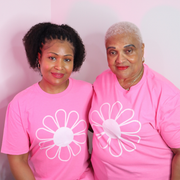 Two women wearing pink t-shirts with white flower designs against a pink background