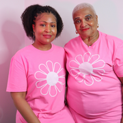 Two women wearing pink t-shirts with white flower designs against a pink background