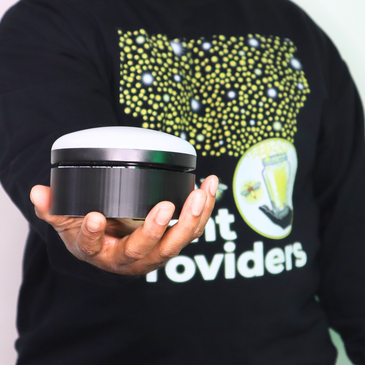 Person holding the Light Provides Wireless Light, wearing a branded black sweatshirt in the background.
